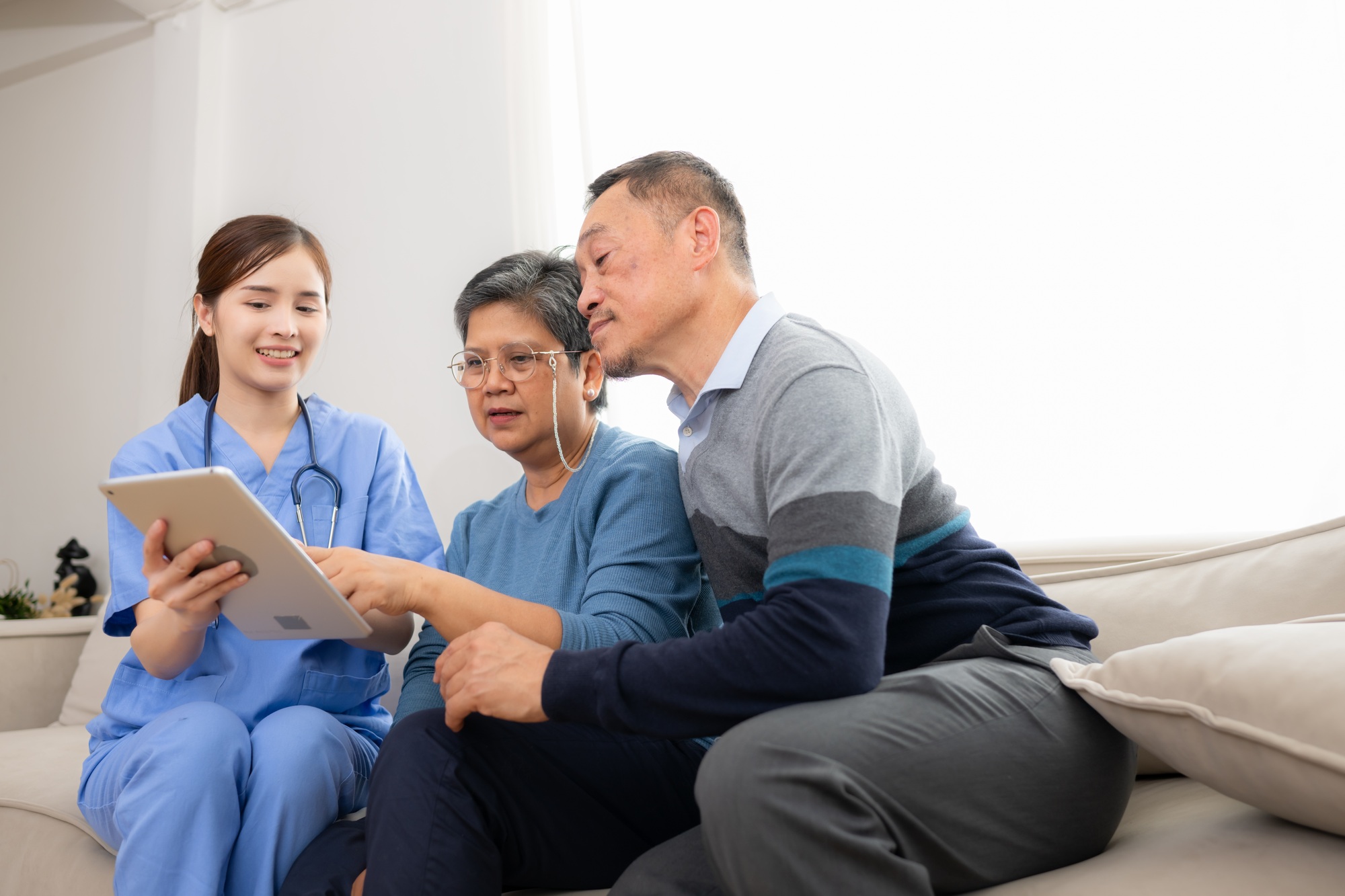 Asian senior patient talking with doctor and nurse on sofa at home