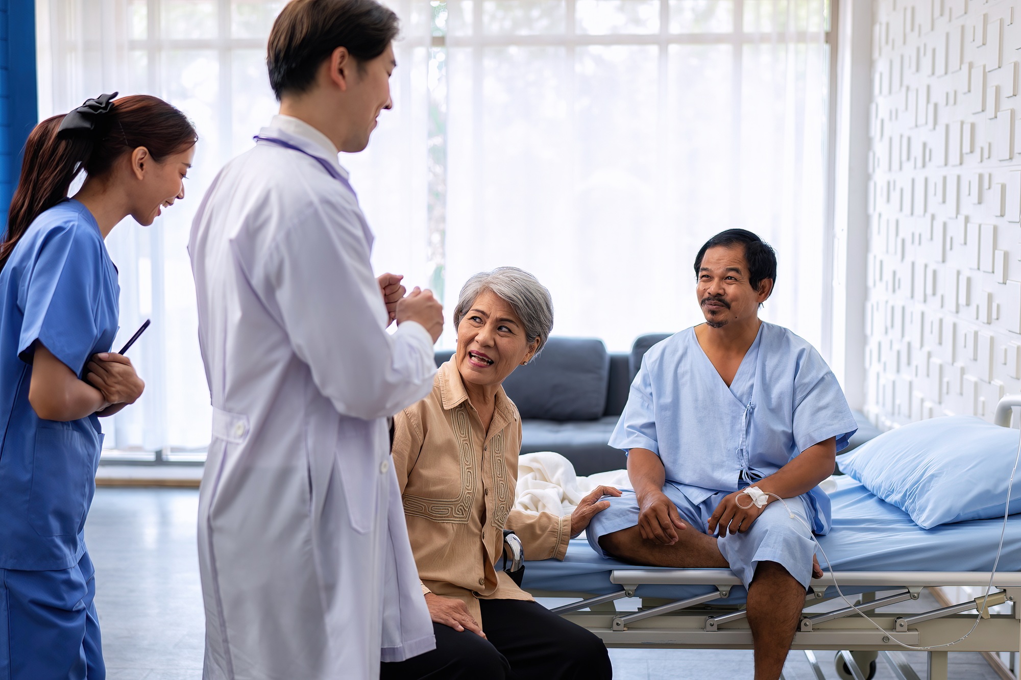 At treatment room patient sitting on bed nurse and doctor congrats him for discharge from hospital