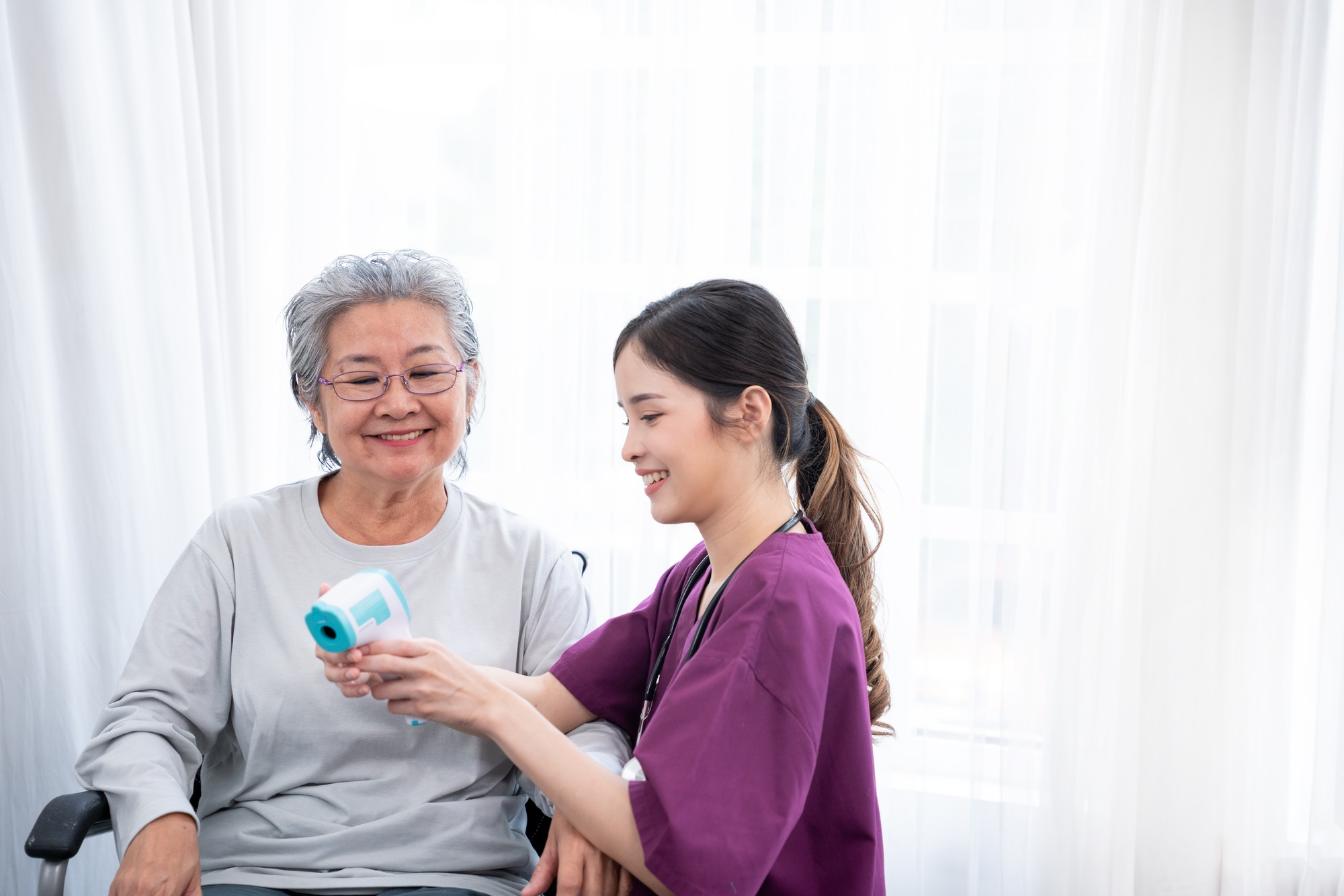 Nurse is caregiver and measuring body temperature senior woman in Home. Home care concept.